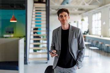 Businessman holding smartphone standing in modern office space