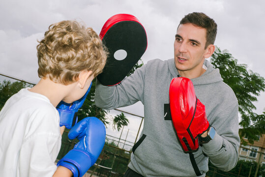 A boxing coach gives a boy a workout in the park