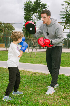 A boxing coach gives a boy a workout in the park