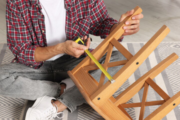 Man using tape measure while repairing wooden stool indoors, closeup