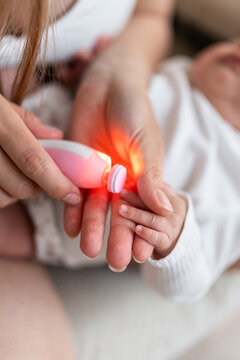 Mother using electric nail trimmer on her baby's nails