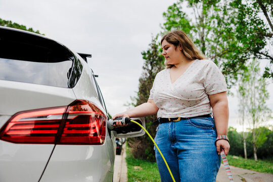 Woman charging electric car at station in city park ugc
