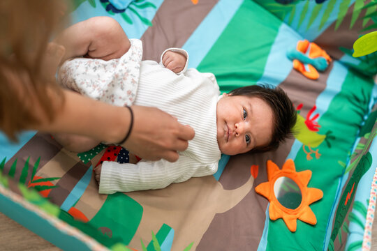 Mother changing her baby clothes on a playmat
