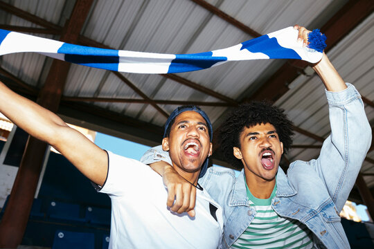 Male sports fans cheering with scarf at stadium