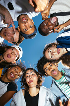 Group of diverse young adults making funny faces against blue sky
