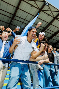 Group of friends cheering and waving flag at stadium