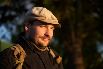 Obraz premium Portrait of a young man wearing a beret looking towards the sun at sunset without sunglasses, you can see from his gesture that the light is bothering his eyes, but he is smiling.
