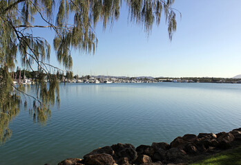Calm ocean at a marina with boats, rocks and trees under a clear blue sky