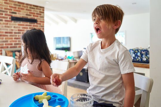 Siblings enjoy snack time with mums in kitchen 
