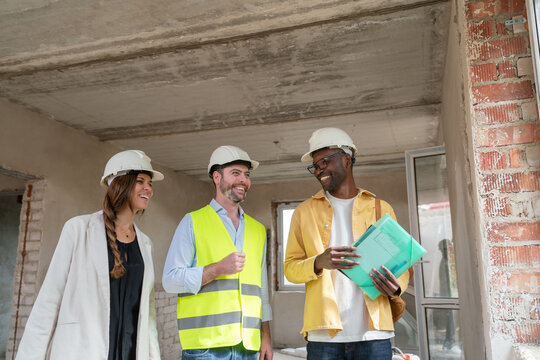Architect Showing House Design To Couple Wearing Hard Hats