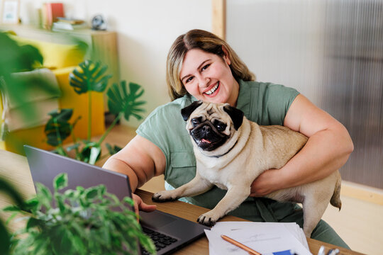 Happy woman working from home and holding her pug