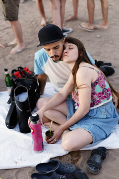 Happy couple relaxing on the beach drinking mate