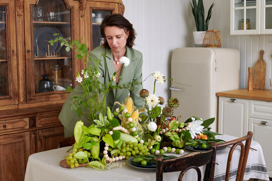 Woman arranging a composition of vegetables and flowers on the table