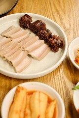 A plate of bossam (boiled pork) and soondae (blood sausage) with assorted banchan (kimchi, pickles, fresh green chillies) at Yeodongsik, a Korean gukbap restaurant in Sydney, Australia