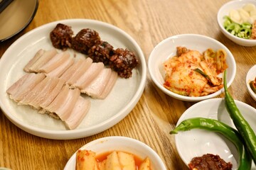 A plate of bossam (boiled pork) and soondae (blood sausage) with assorted banchan (kimchi, pickles, fresh green chillies) at Yeodongsik, a Korean gukbap restaurant in Sydney, Australia