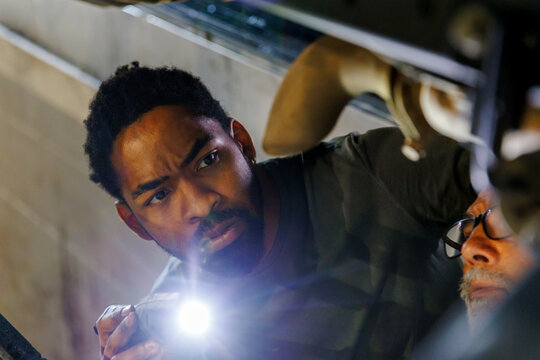 Technician examining vehicle with torchlight at auto repair shop