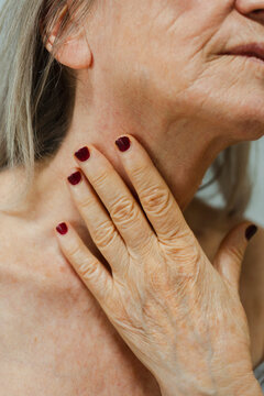 Crop of anonymous senior woman touching her neck