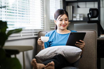 Portrait of a woman using tablet checking email or news online while sitting on sofa at home. Searching for friends in internet social networks or working on computer. Copy space.