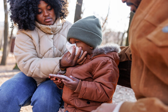 Mother wiping nose of son using mobile phone