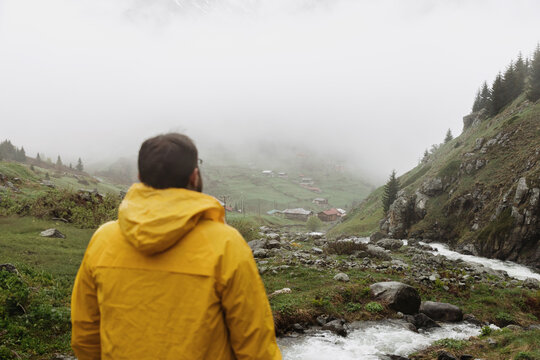 Man in Yellow Raincoat Overlooking Mountain Stream
