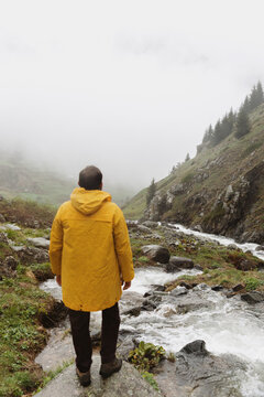 Man in Yellow Raincoat Overlooking Mountain Stream
