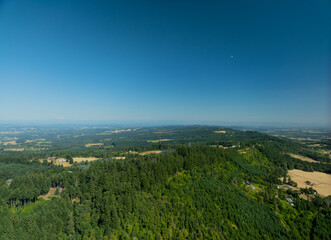 Fototapeta premium Drone shot. Under the blue sky there is a high mountain with a dense green forest. There are beautiful houses on the edges. Hilly area, lots of greenery. The beauty of nature, ecology.