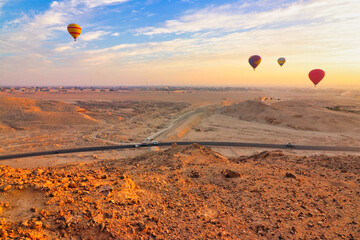 Hot Air balloons rises over the reddish ochre coloured desert landscape with views of the vast...