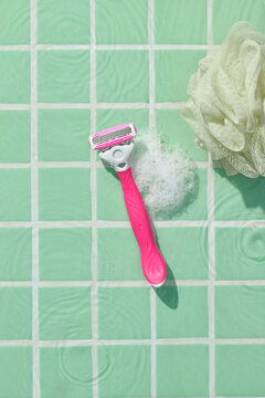 Pink Razor with Foam and Loofah on Green Tiles Background