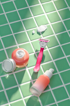 Three colorful razors and shaving cream on a green tiled surface