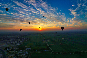 A glowing sun rises over the fertile fields on the banks of the nile against a cloud streaked sky with silhouettes of Hot Air balloons operated by Luxor tour companies near Luxor,Egypt 