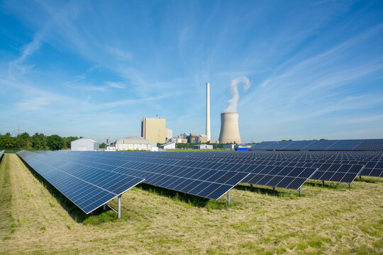 Field with solar panels and a coal-fired power station