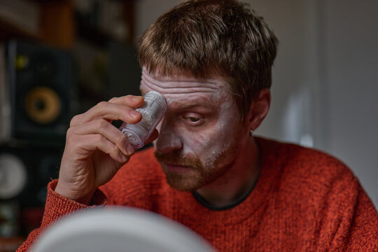 Young man applying clay mask on his face in front of a mirror