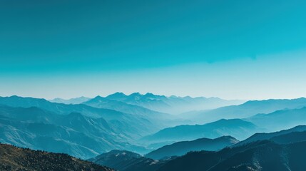 Obraz premium Layered blue mountain ranges fade into a misty valley under a clear teal sky during a bright day.