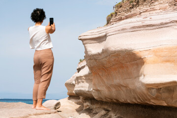 Back shot of woman taking photos with her smartphone on the rock