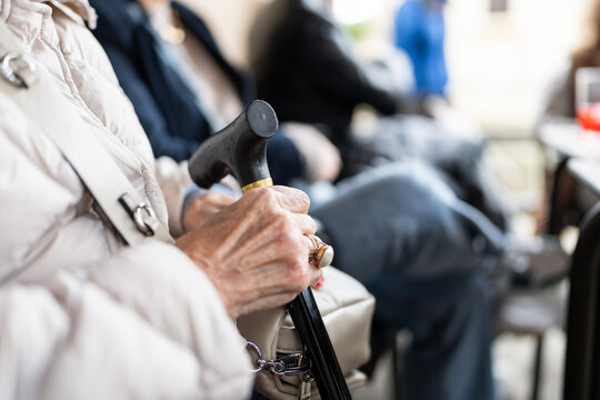 Elderly woman holding walking stick while sitting outdoors