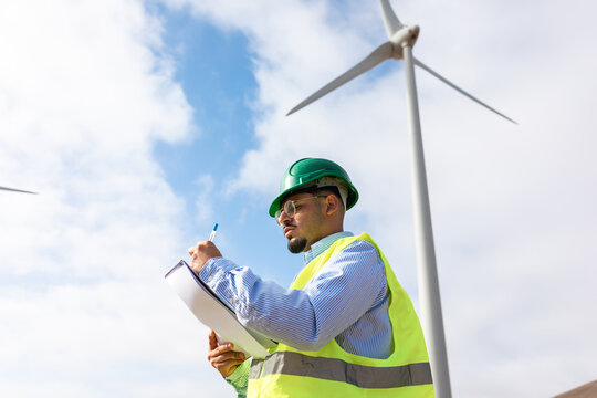 A wind turbine technician makes notes at a windmill farm.
