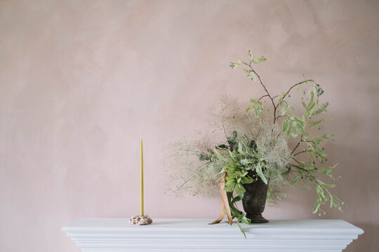 Minimalist mantel decor with candle and floral vase.