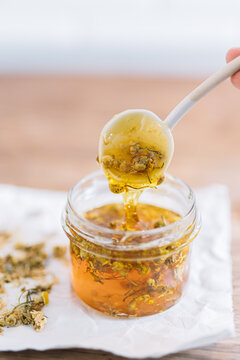 Spoon with honey and chamomile flowers over glass jar.
