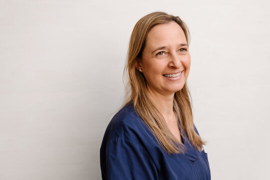 Woman in blue scrubs smiling against plain background
