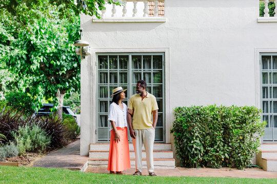 Happy couple standing arm in arm in front of house
