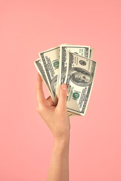 Hand Holding US Dollar Bills Against Pink Background. 