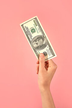 Hand Holding US Dollar Bill Against Pink Background. 