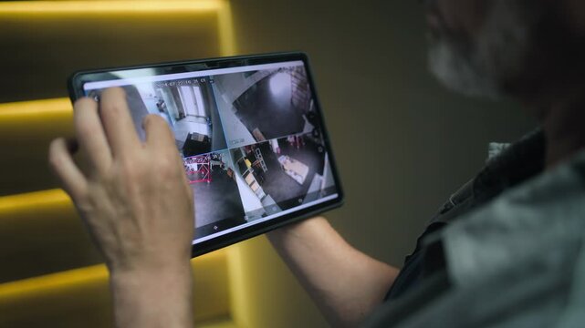 Professional installer watches security cameras in stylish office using tablet computer. View from surveillance cameras displayed on tablet screen. Monitoring and tracking. CCTV system and privacy.