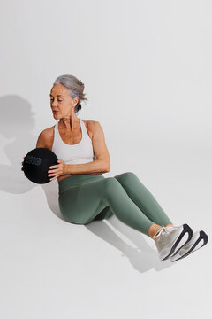 Senior woman doing crunches with medicine ball on white background. 