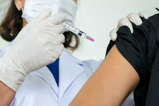 Doctor's hand holding syringe and injecting vaccine into woman's arm at hospital. Health and medical concept.