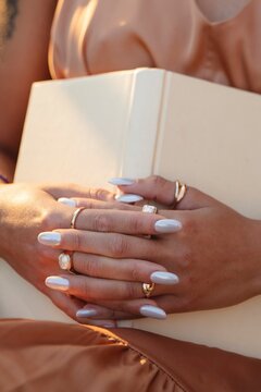 Close-up of Hands Holding a Book with White Nail Polish and Rings