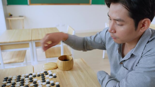 Asian young man playing board game Go during competition in community. 