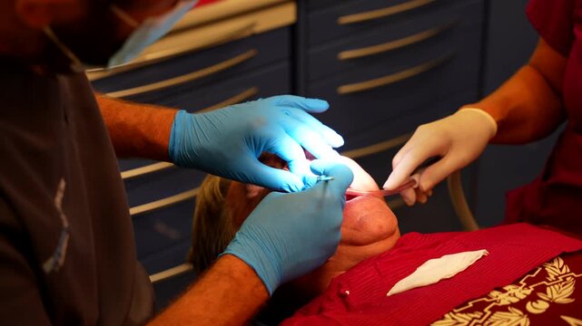 Dentist adjusts screws on a patient's denture while assistant uses saliva ejector due to blood