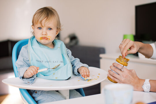 Toddler Eating in High Chair looking at camera grumpy