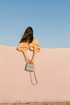 Woman Leaning on Wall with Small Grey Purse in Hands